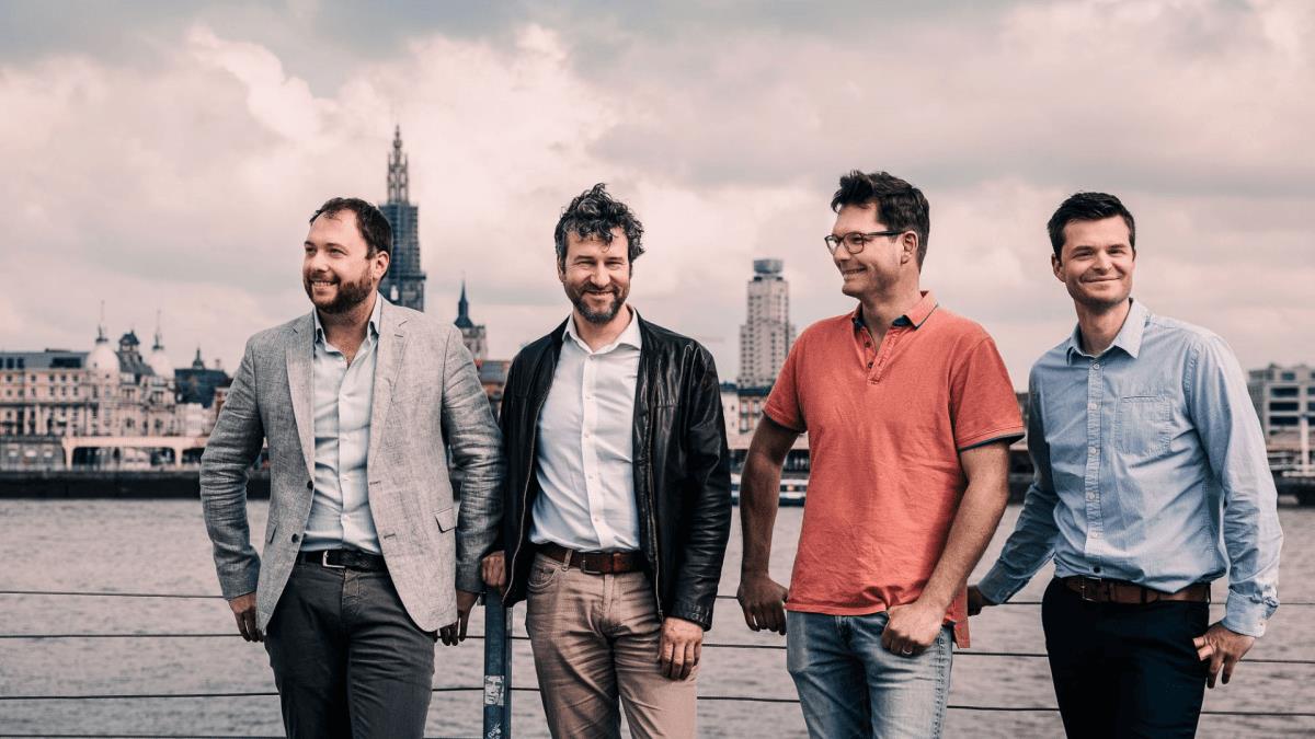 Four men in business casual attire stand before a body of water.