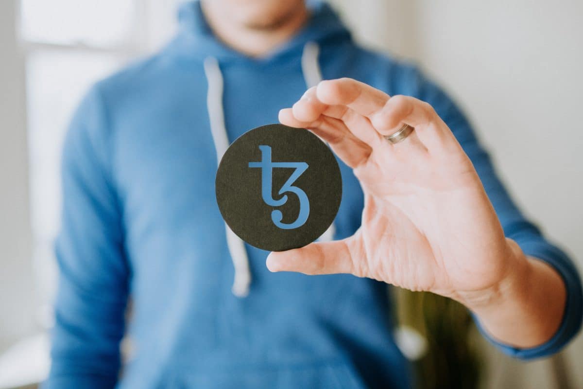 A man holding a tezos logo for Rarible NFT marketplace