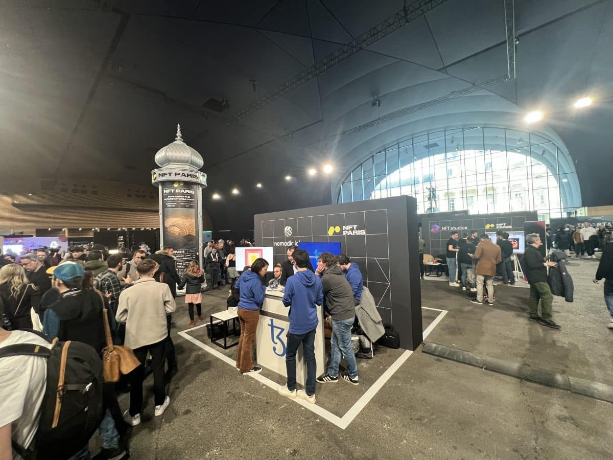 people standing around a booth at an NFT conference at NFT Paris 2023